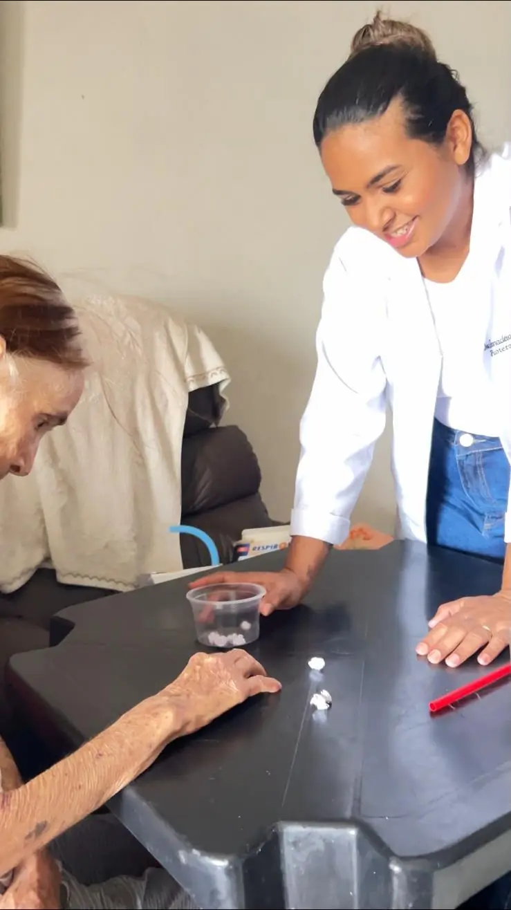 Paciente idosa em atividade de coordenação das mãos, com a fisioterapeuta ao lado