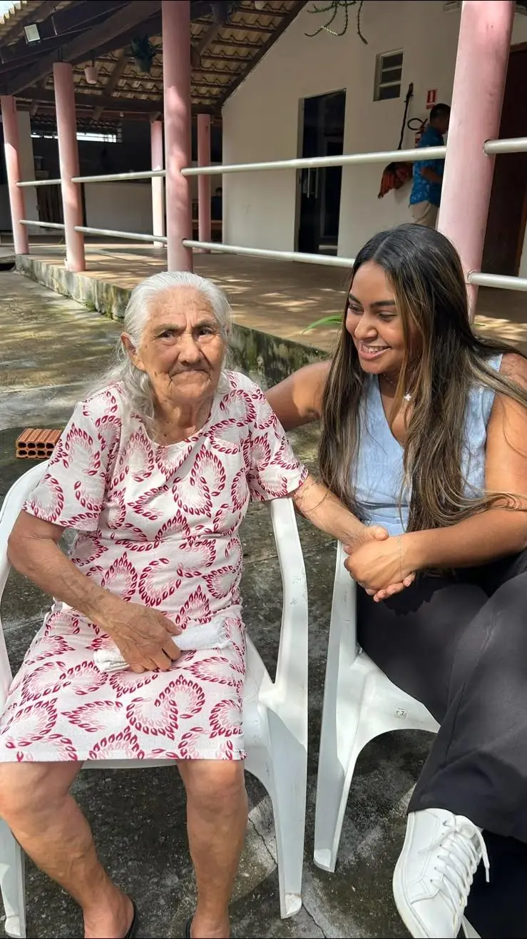 Dra. Francicléia sentada ao lado de uma paciente idosa, de mãos dadas